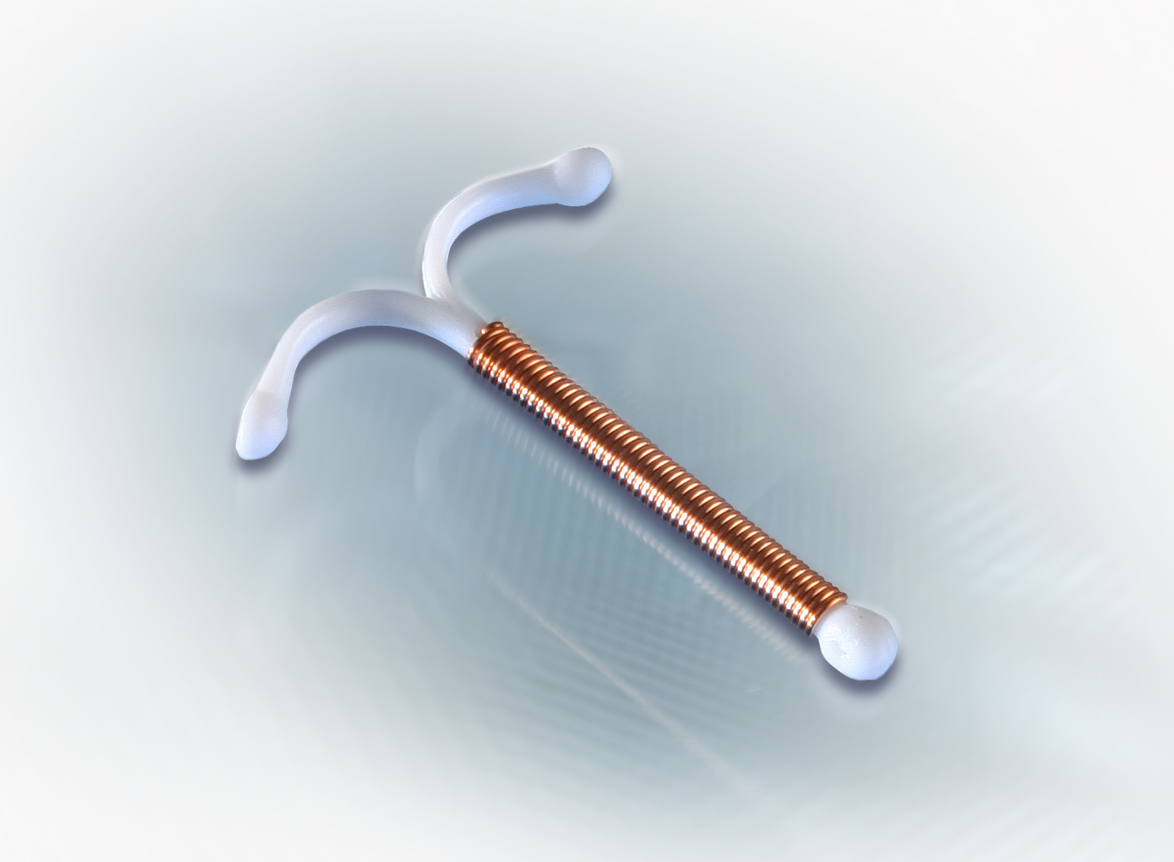 Eine Kupferhaltige Intrauterinspirale, auch bekannt als Goldspirale, vor einem sanft beleuchteten Hintergrund.