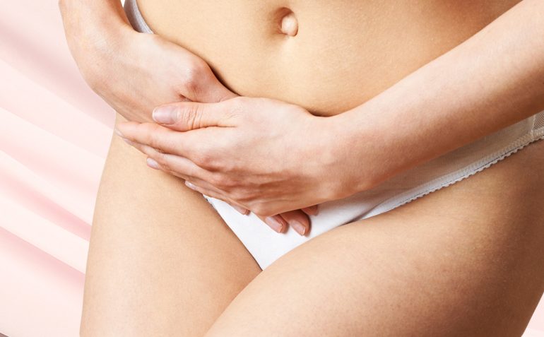 Eine Person, die nur bis zum Unterbauch sichtbar ist, hält ihre Hände zwischen den Beinen, was ein häufiges Bild für das Thema Inkontinenz ist. Sie trägt weiße Unterwäsche und steht vor einem pastellfarbenen Hintergrund, was auf die Intimität und Sensibilität des Themas hinweist.