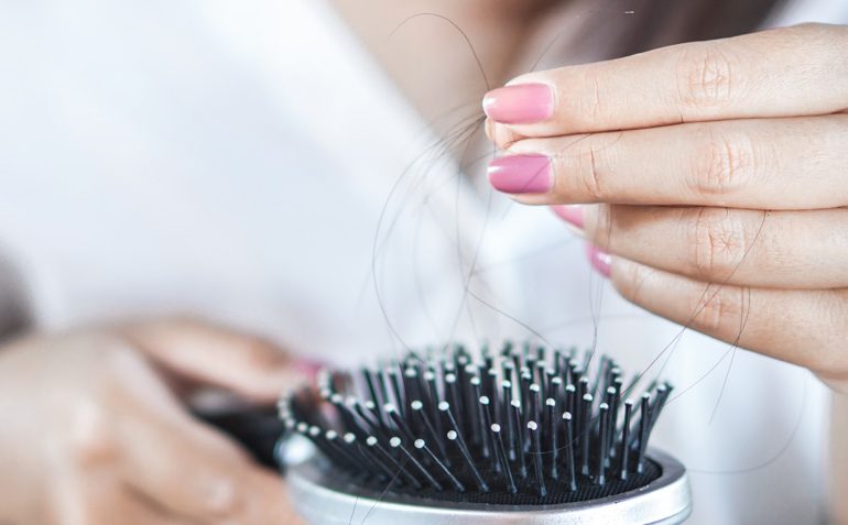 Eine Frau kämmt sich mit einer Bürste die Haare, um Haarausfall zu bemerken.