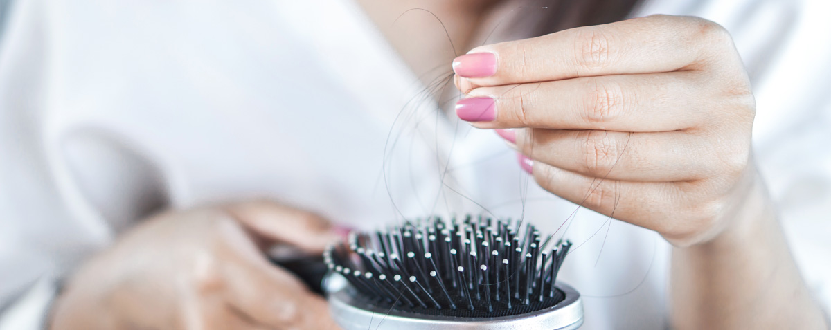 Eine Frau kämmt sich mit einer Bürste die Haare, um Haarausfall zu bemerken.