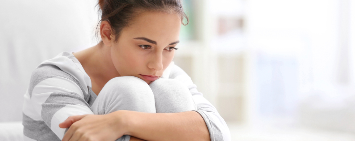 Eine Frau sitzt mit den Händen auf den Knien auf einem Bett und zeigt Anzeichen von Lichen sclerosus.